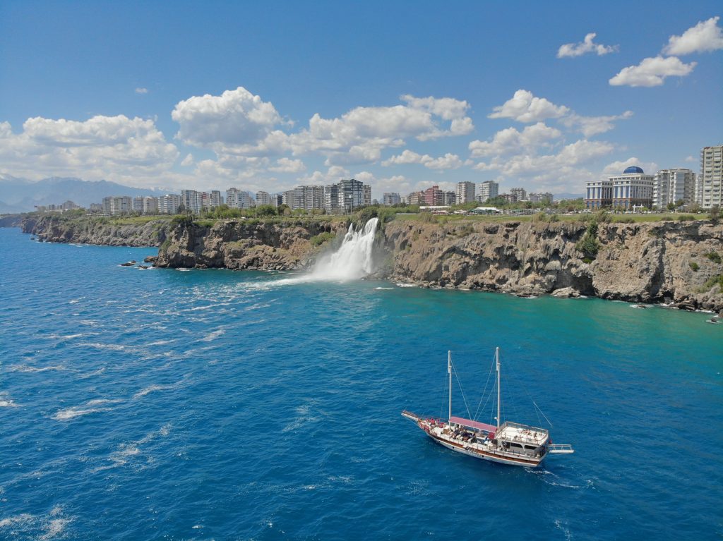 A scenic aerial view of Duden Waterfall cascading into the sea with a sailboat nearby in Antalya, Turkey.
